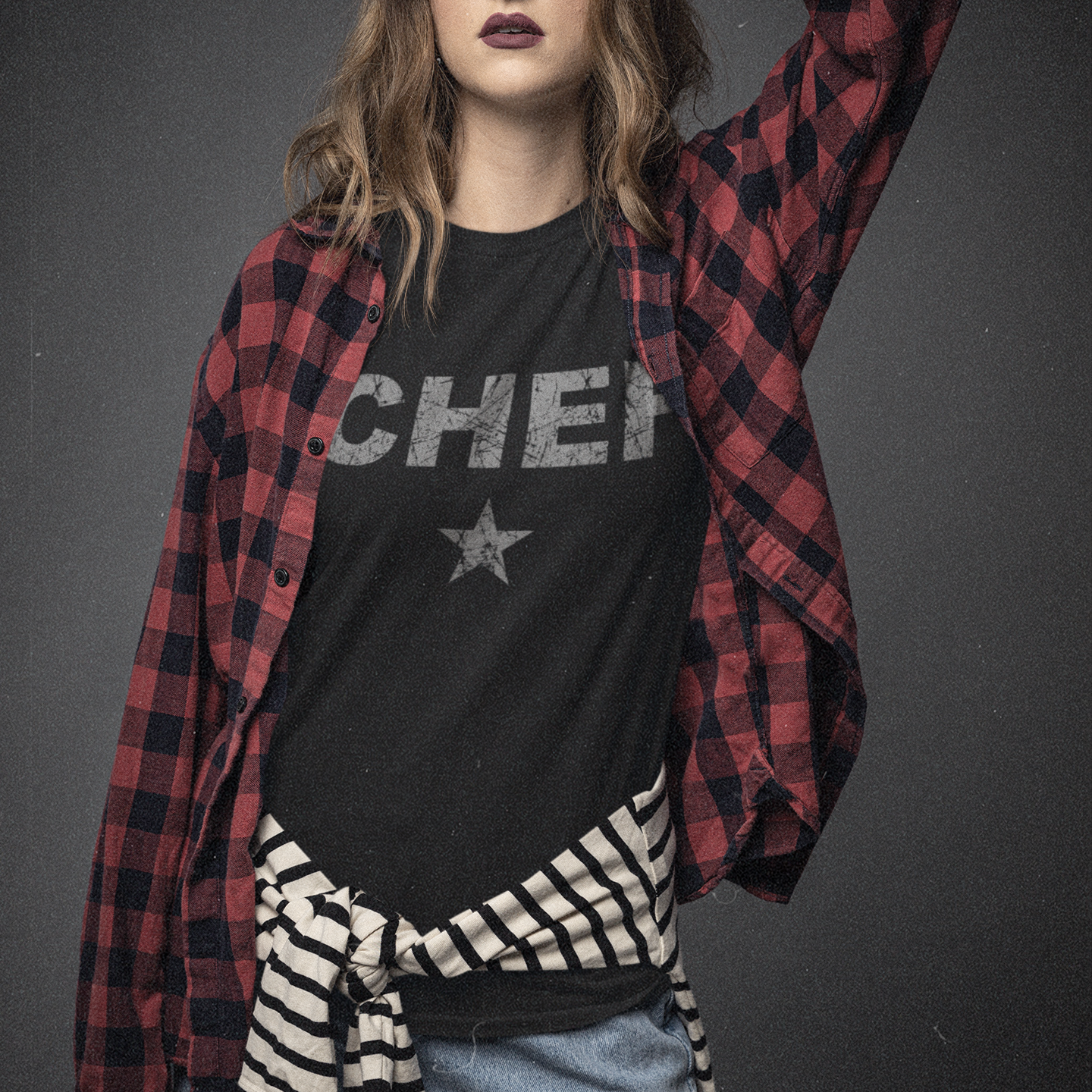 Person wearing a black t-shirt with text and a red plaid shirt over it, on a dark background