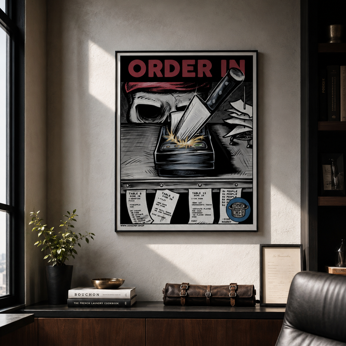 A framed vintage-style office poster reading 'ORDER IN' hangs on a wall in a modern office setting with a desk, chair, and shelving visible.