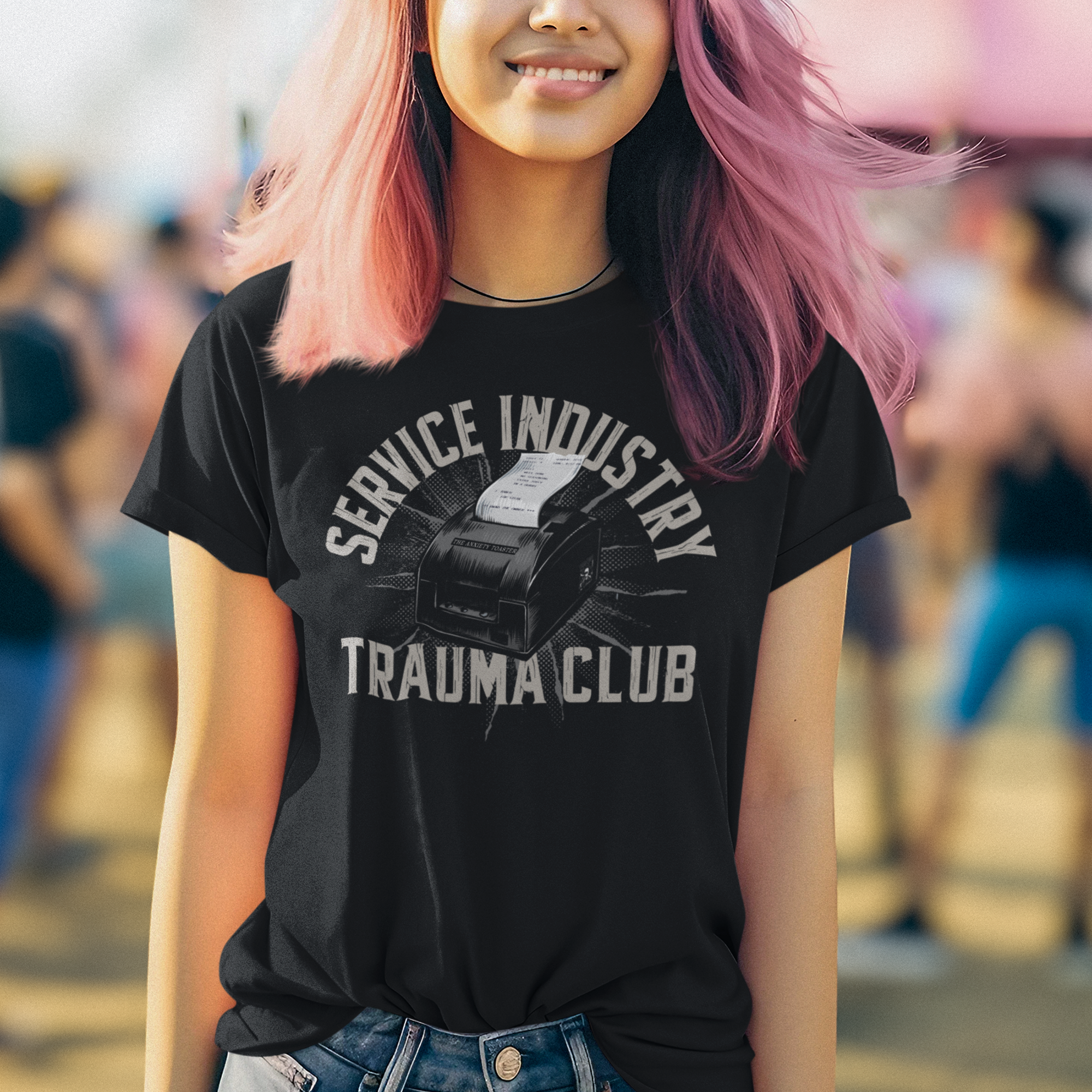 Person with pink hair wearing a black t-shirt with text and graphics, standing in a crowd.