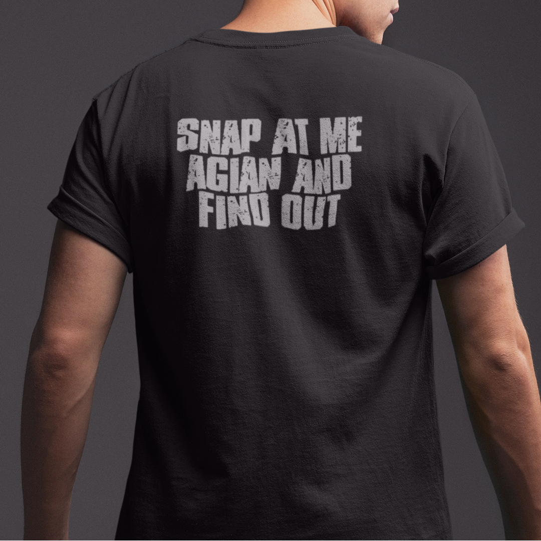 A man shown from the back wearing a black t-shirt with the text 'SNAP AT ME AGIAN AND FIND OUT' printed in distressed white letters on the back, set against a dark gray studio background.