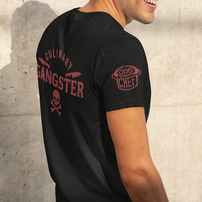 A man wearing a black t-shirt with red graphic prints on the back and sleeve, standing against a textured concrete wall.