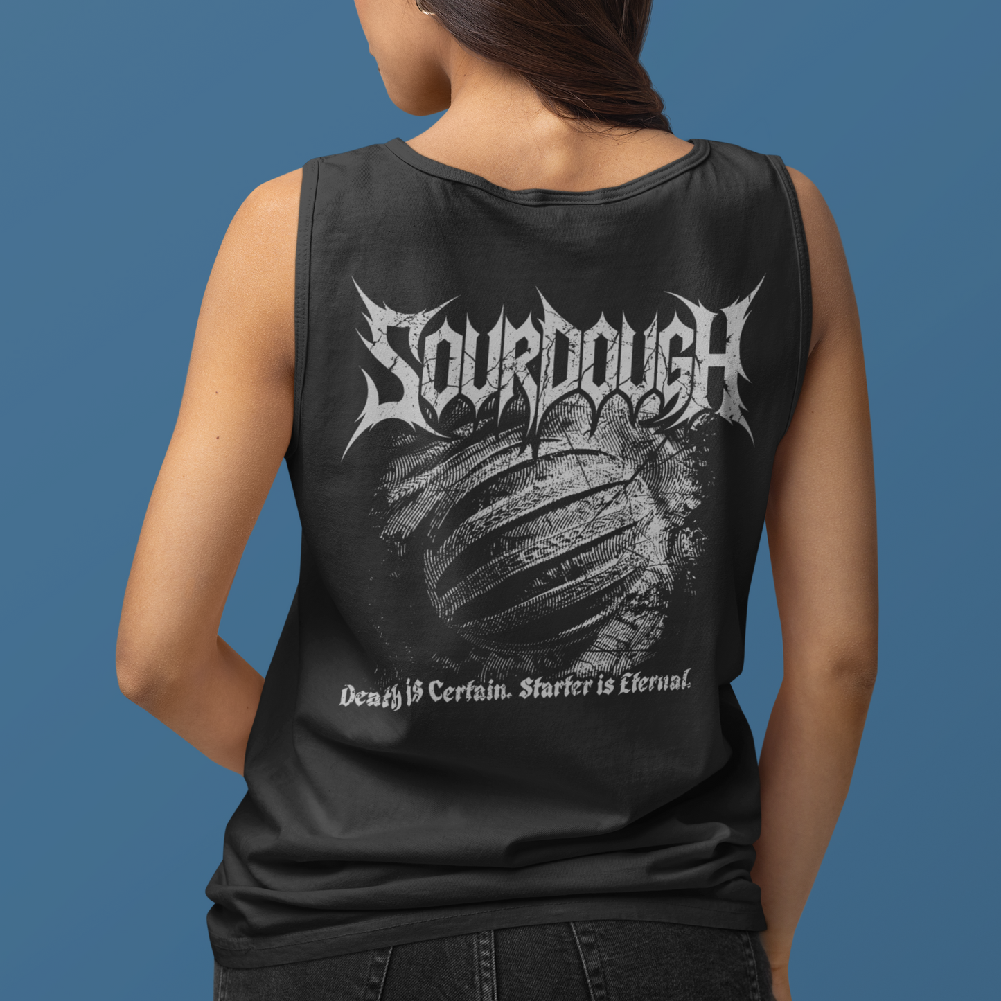 A woman shown from the back wearing a black sleeveless tank top with a large white 'Sourdough' band graphic and distressed text on the back, against a solid blue studio background.