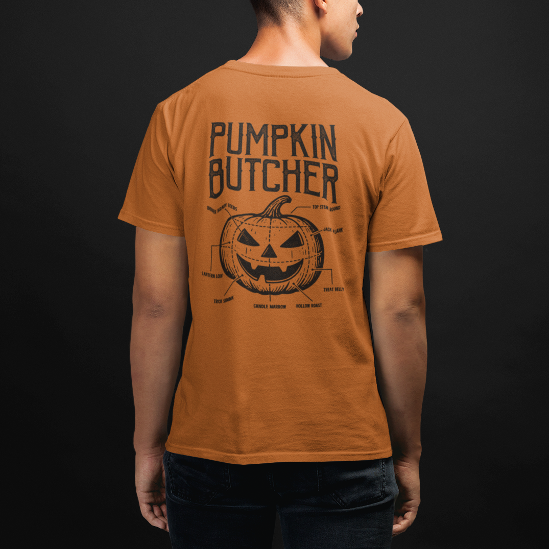 A man viewed from behind wearing an orange t-shirt with a black graphic print that reads 'PUMPKIN BUTCHER' above a pumpkin illustration, set against a dark studio background.
