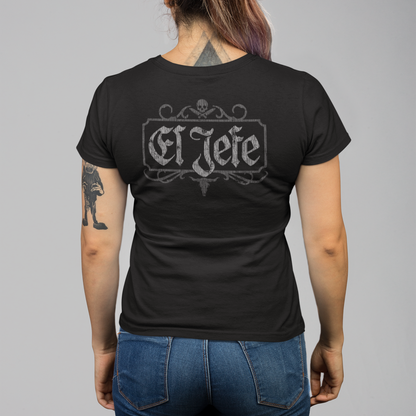 A woman viewed from the back wearing a black short-sleeve t-shirt with a gray 'El Jefe' gothic-style graphic on the back, paired with blue jeans, against a solid gray studio background.