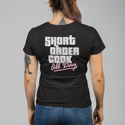 A woman viewed from behind wearing a black t-shirt with a graphic that reads 'SHORT ORDER COOK All Day' in white and pink, paired with blue jeans, against a solid gray background.