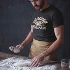 Man in a 'Big Dough Energy' t-shirt kneading dough on a flour-dusted table.