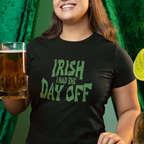 Person wearing a black t-shirt with green text, holding a glass of beer against a green curtain background.