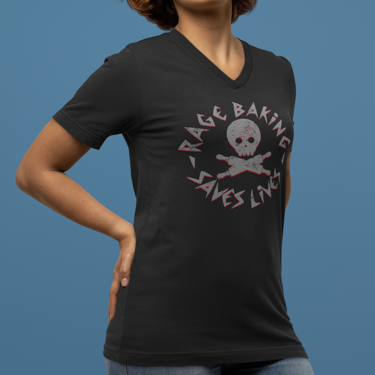 A woman wearing a black V-neck t-shirt with a distressed graphic that reads 'RACE BAKING SAVES LIVES' around a skull and crossbones, posed against a solid blue background.