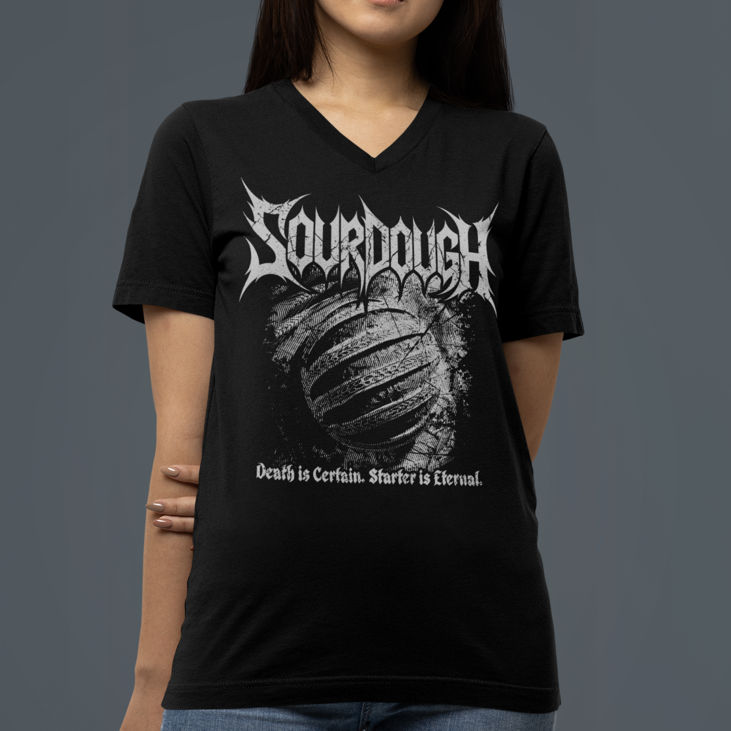 A woman wearing a black V-neck t-shirt with a white 'Sourdough' band graphic on the front, paired with blue jeans, set against a solid dark gray background.