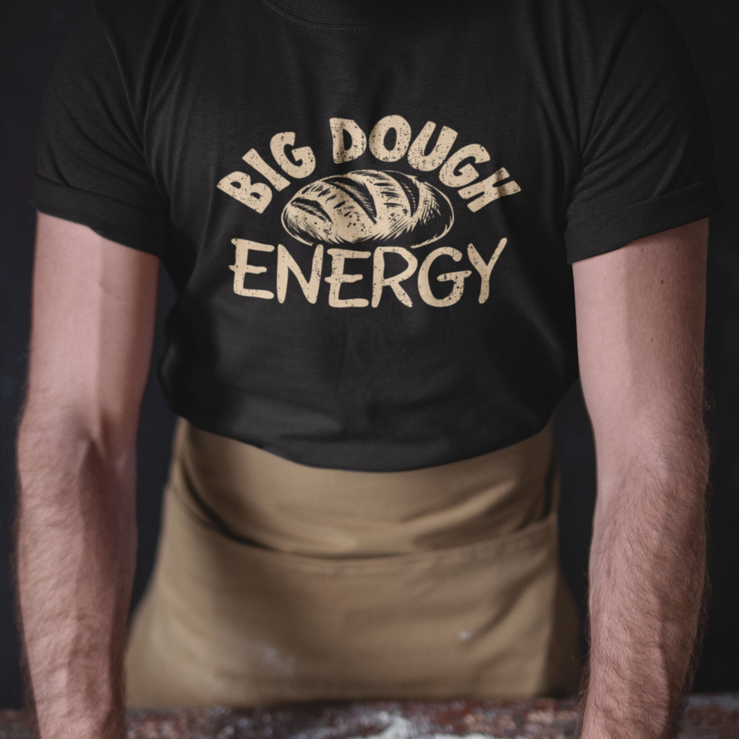 Person wearing a black t-shirt with 'Big Dough Energy' text, rolling dough in a flour-dusted kitchen.