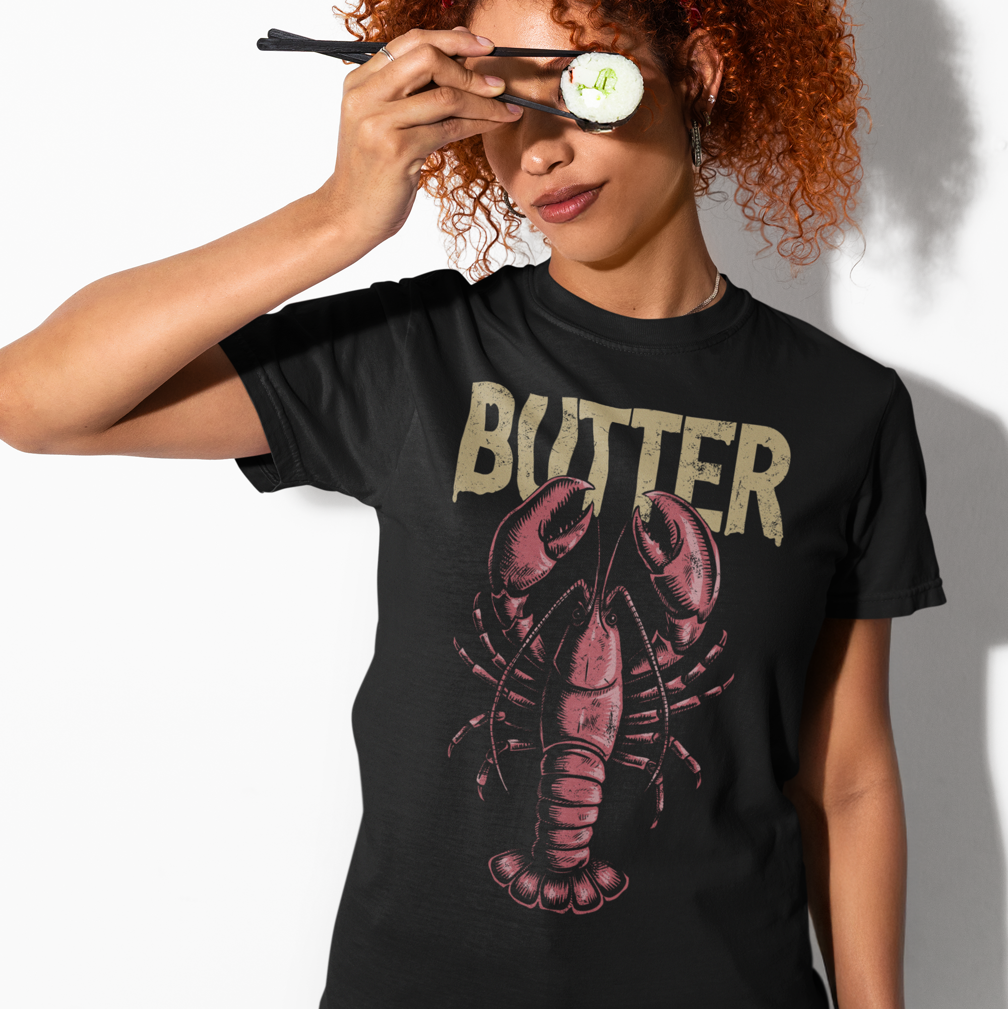 Person wearing a black t-shirt with a lobster graphic and 'BUTTER' text, holding sunglasses.