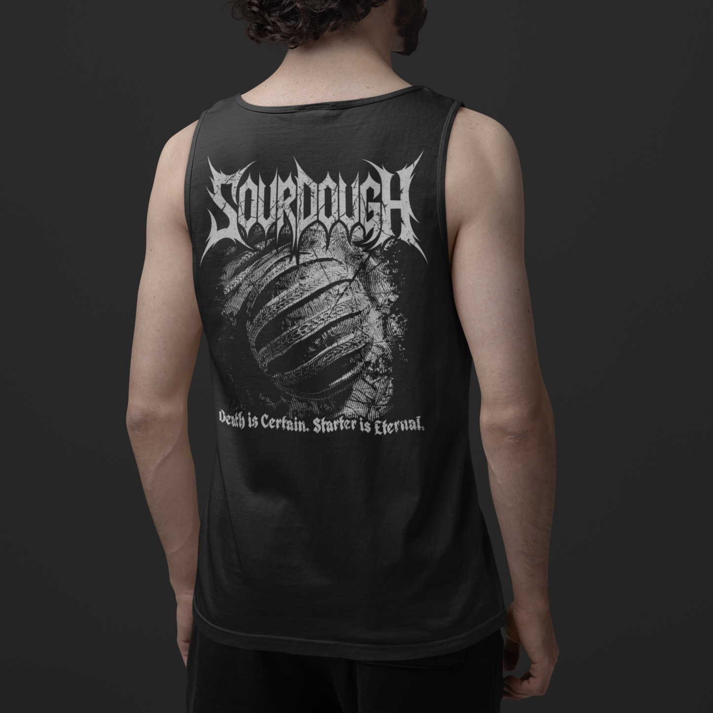 A man viewed from behind wearing a black sleeveless tank top with a large white 'Sourdough' band graphic and text on the back, paired with black shorts against a dark gray studio background.