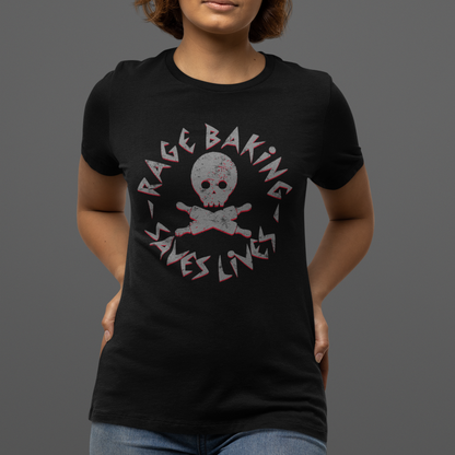 A woman wearing a black short-sleeve graphic t-shirt with a distressed pink and white 'Rage Baking Saves Lives' skull and crossbones design, paired with blue jeans, against a solid dark gray background.