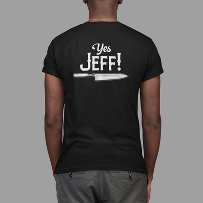 A man viewed from behind wearing a black t-shirt with a white graphic that reads 'Yes JEFF!' above a knife illustration, paired with gray pants, against a solid gray background.