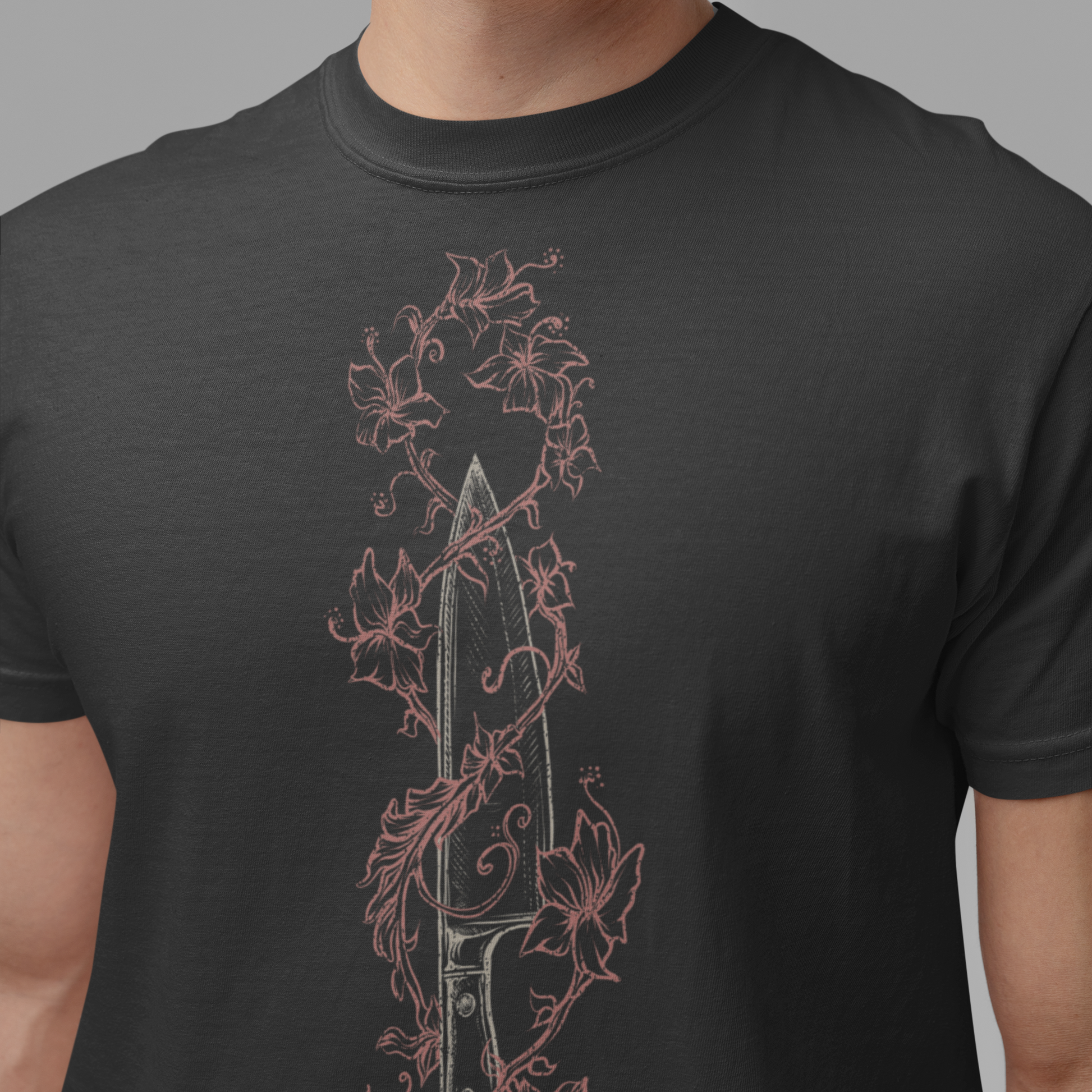 A close-up of a person wearing a dark charcoal gray t-shirt with a vertical graphic print of a dagger entwined with pink floral vines.