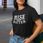 Person wearing a black t-shirt with 'MISE over MATTER' text and a white cap in an indoor setting.