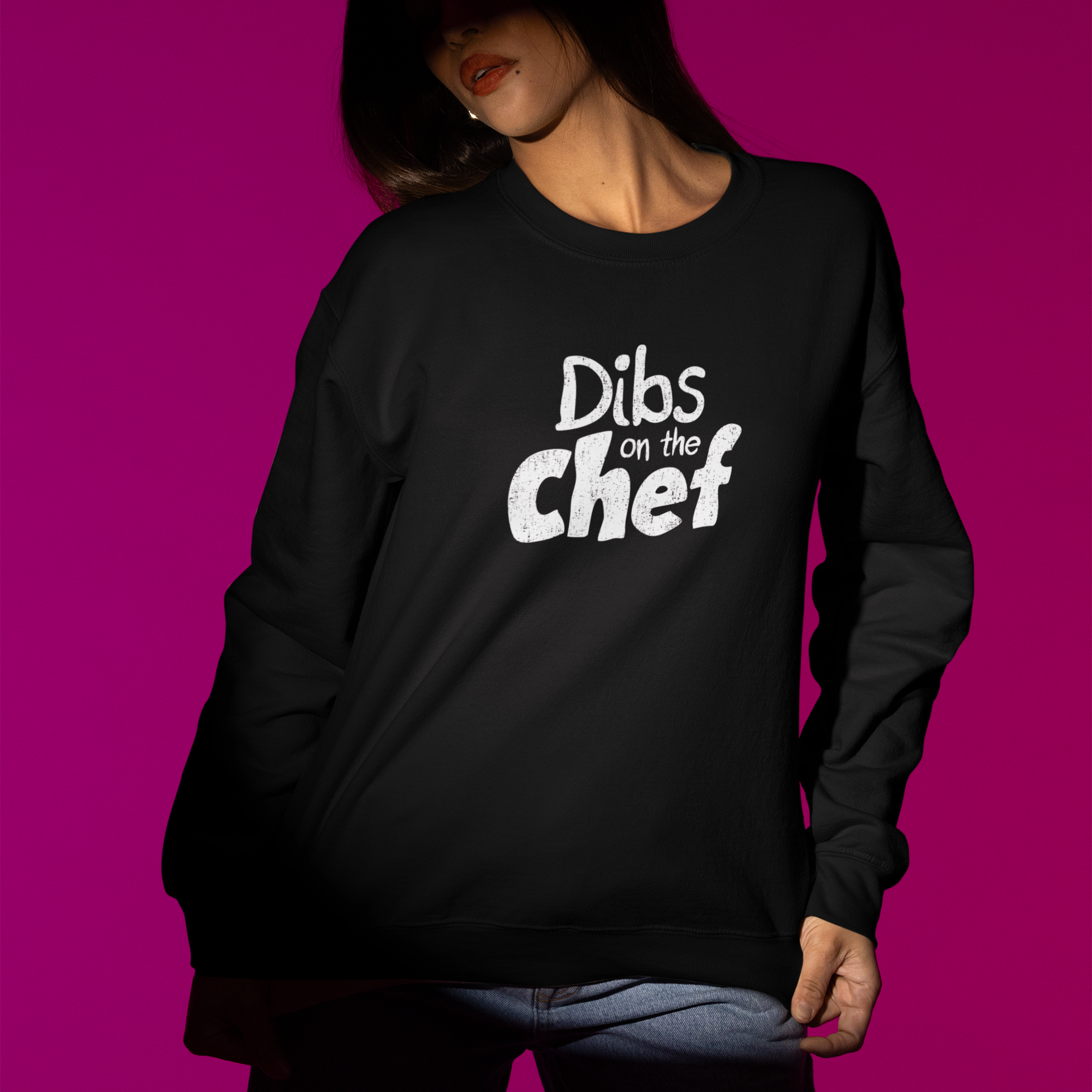 Person wearing a black sweatshirt with 'Dibs on the Chef' text against a pink background