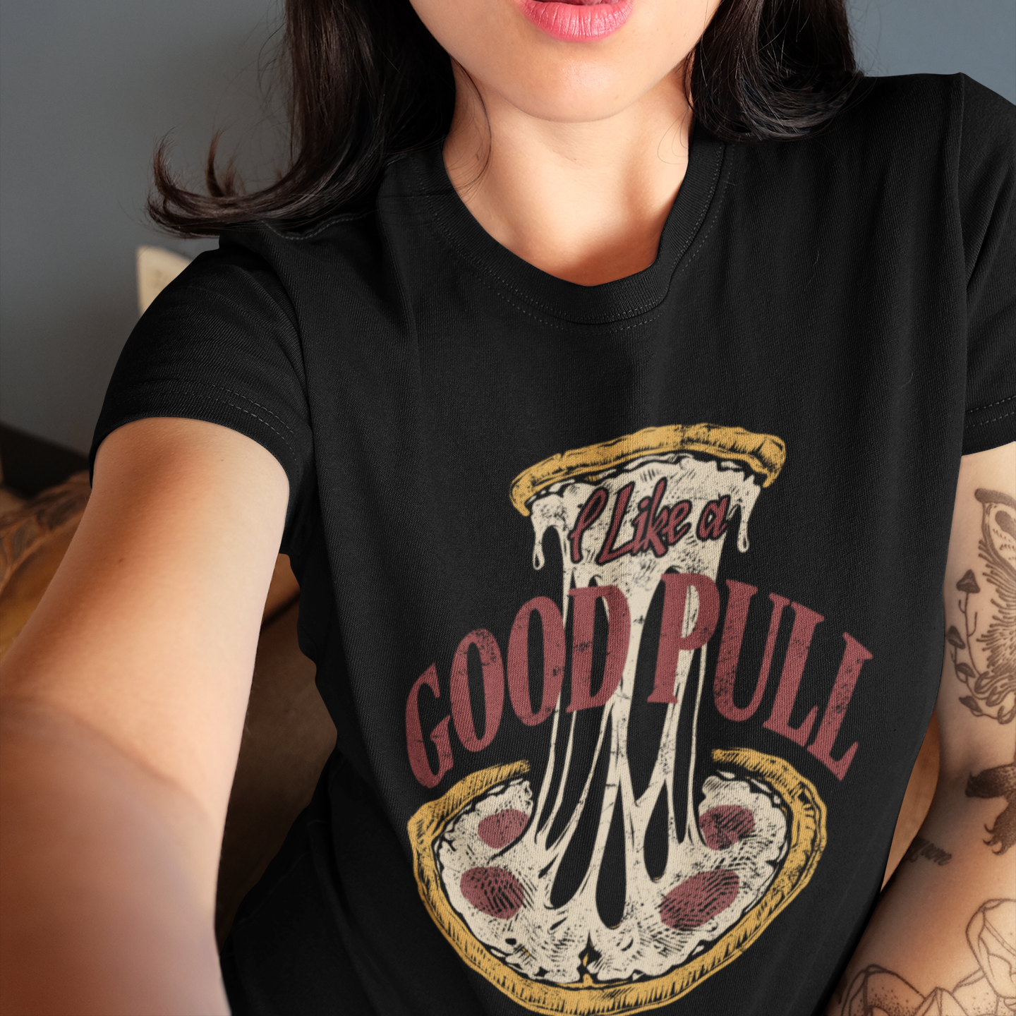 A woman wearing a black graphic t-shirt with a pizza-themed print that reads 'I Like a GOOD PULL'.