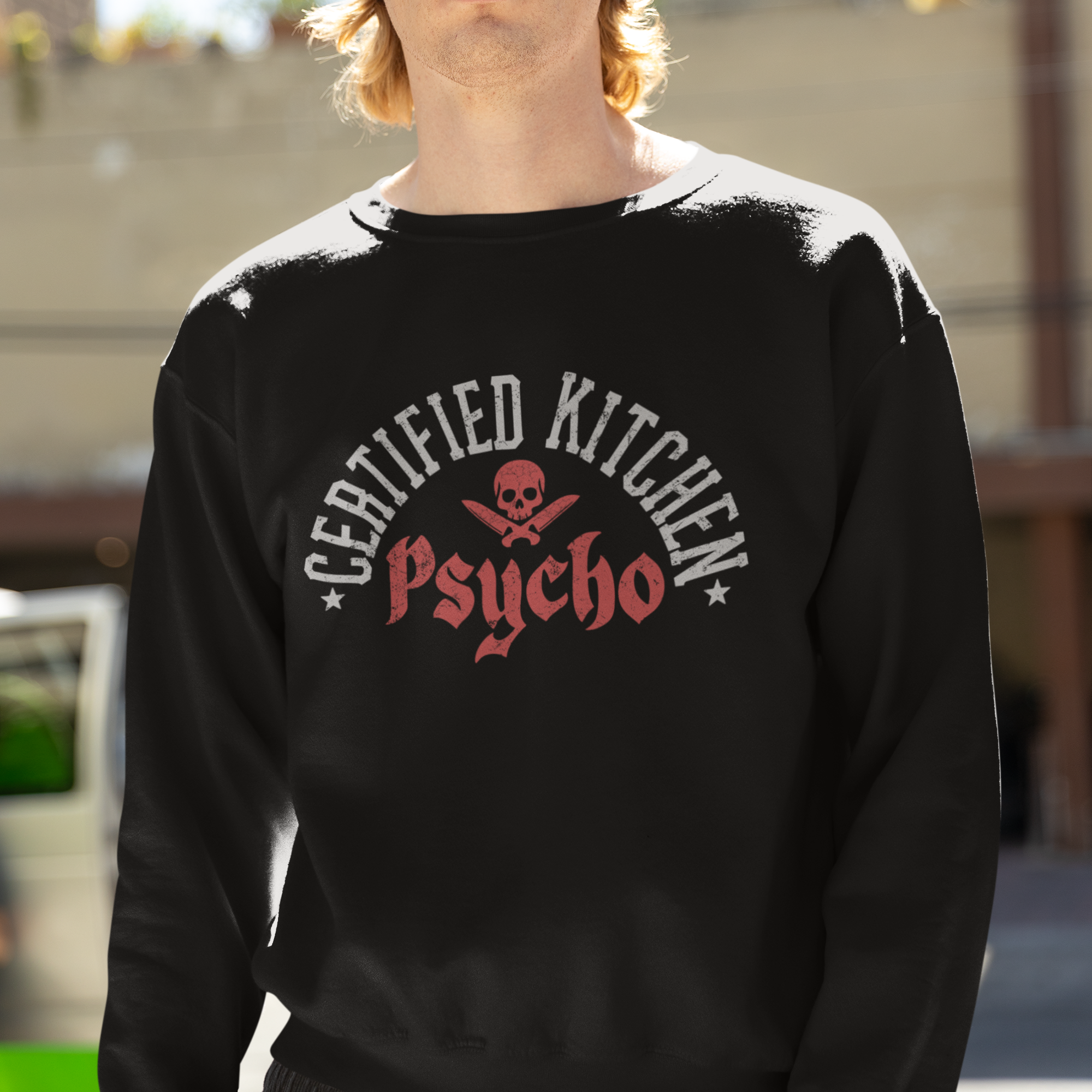 Person wearing a black sweatshirt with 'Certified Kitchen Psycho' text and skull design outdoors.