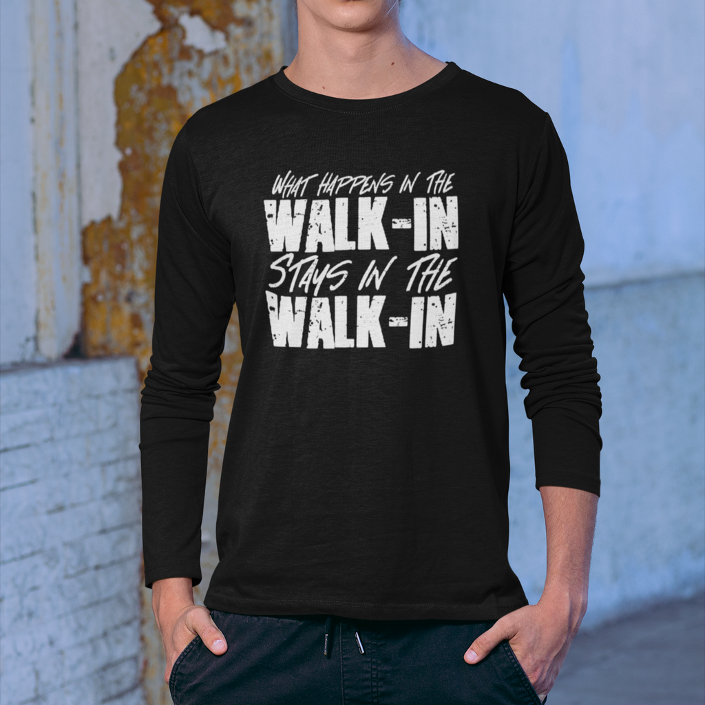 Person wearing a black long-sleeve shirt with text, standing against a textured wall.
