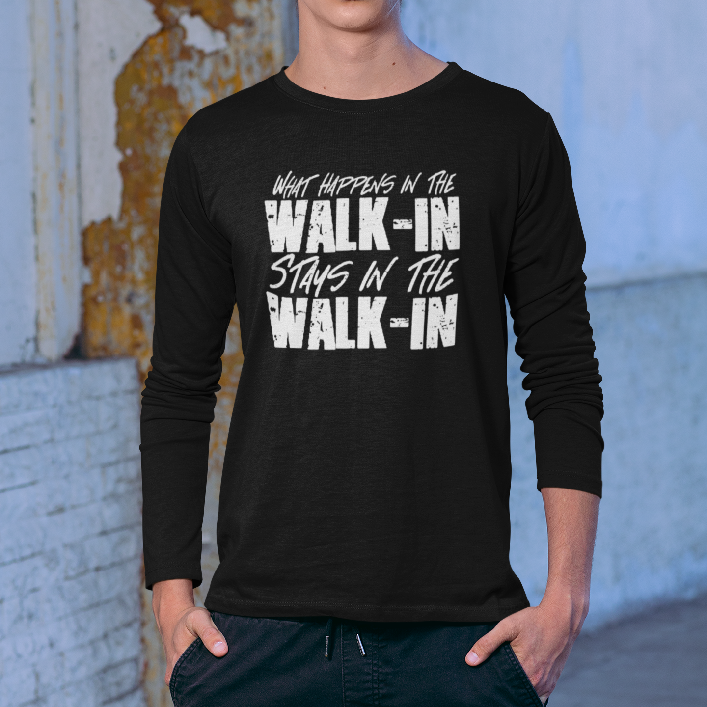 Person wearing a black long-sleeve shirt with text, standing against a textured wall.
