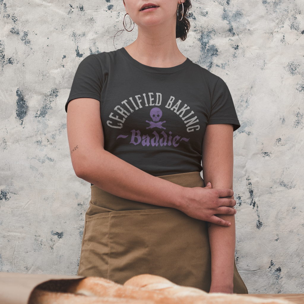 Person wearing a 'Certified Baking Buddy' t-shirt standing behind a table with bread, against a textured wall.