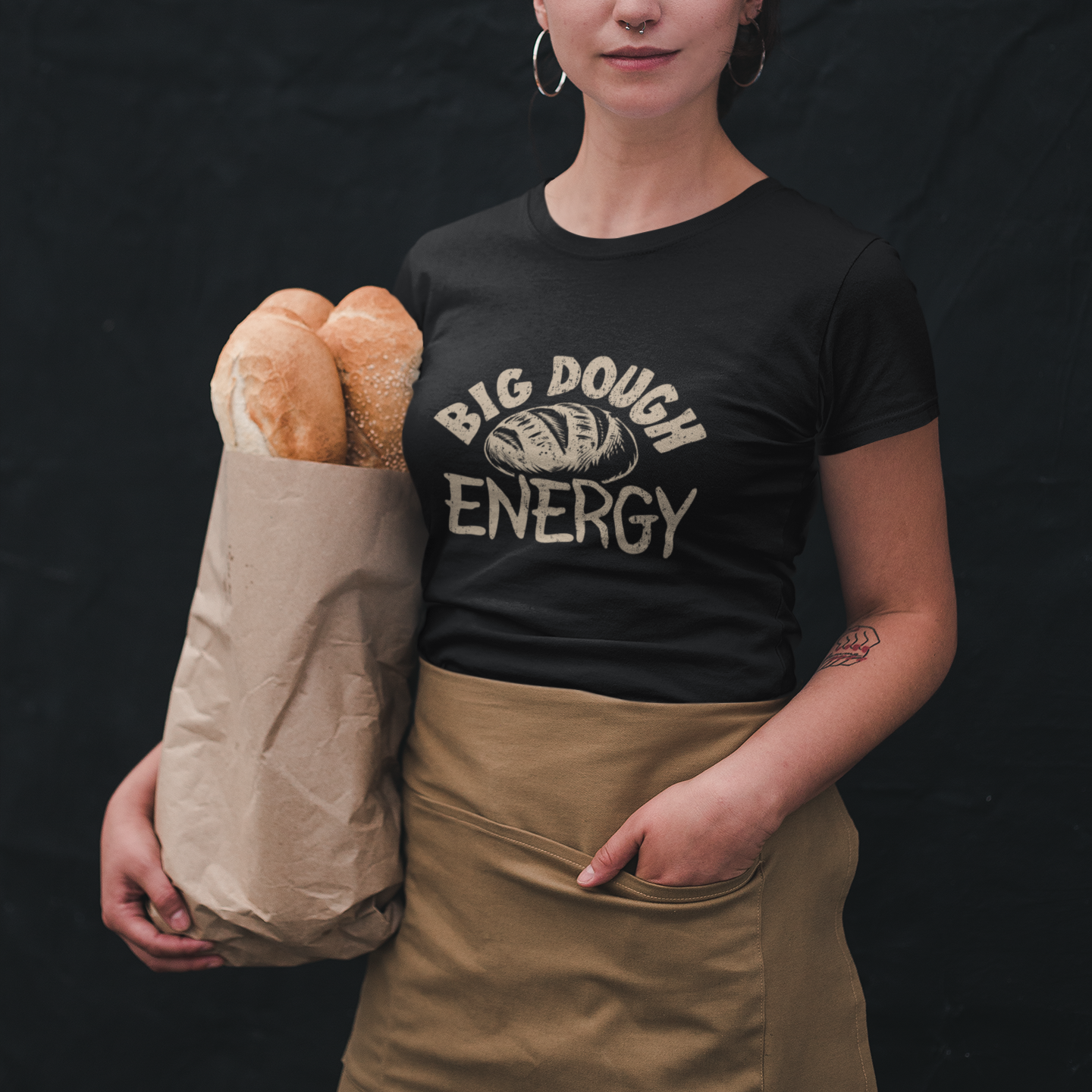 Woman holding a bag of bread wearing a black t-shirt with 'Big Dough Energy' text on a dark background