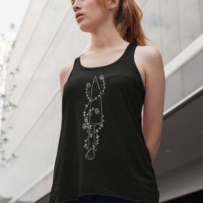 A woman wearing a black tank top with a white floral dagger graphic, photographed outdoors against a modern glass building.