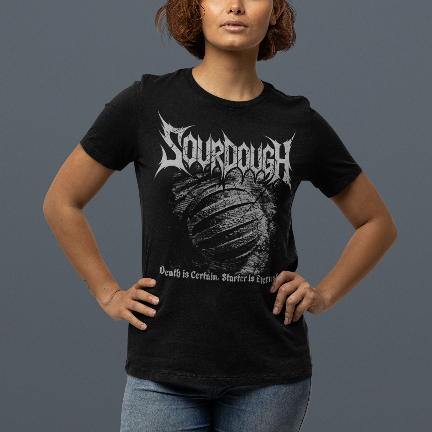 A woman modeling a black short-sleeve graphic t-shirt with a white 'Sourdough' band logo and a distressed bread crust design on the front, set against a solid dark gray studio background.
