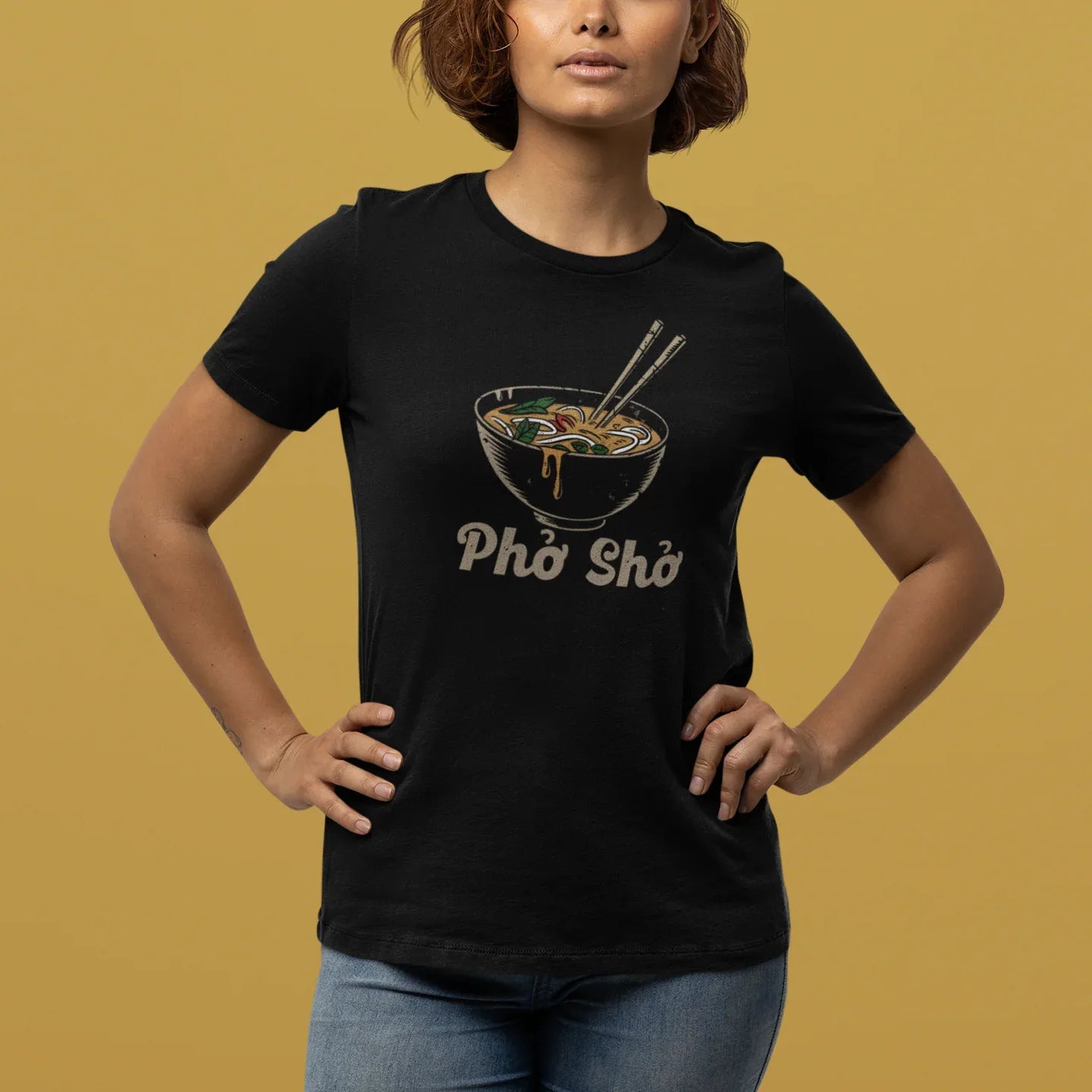 Person wearing a black t-shirt with a graphic design and text on a mustard yellow background