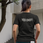 Person wearing a black t-shirt with 'YES CHEF!' text outdoors.
