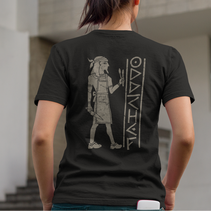 A woman viewed from behind wearing a black t-shirt with a large gray graphic of an ancient Egyptian figure and the word 'MAURITIUS' printed on the back, standing outdoors in front of a modern building.