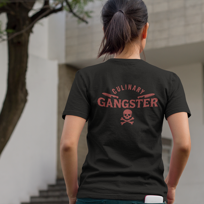 A woman viewed from behind wearing a black t-shirt with a red graphic that reads 'CULINARY GANGSTER' and a skull and crossbones, standing outdoors in front of a modern building.
