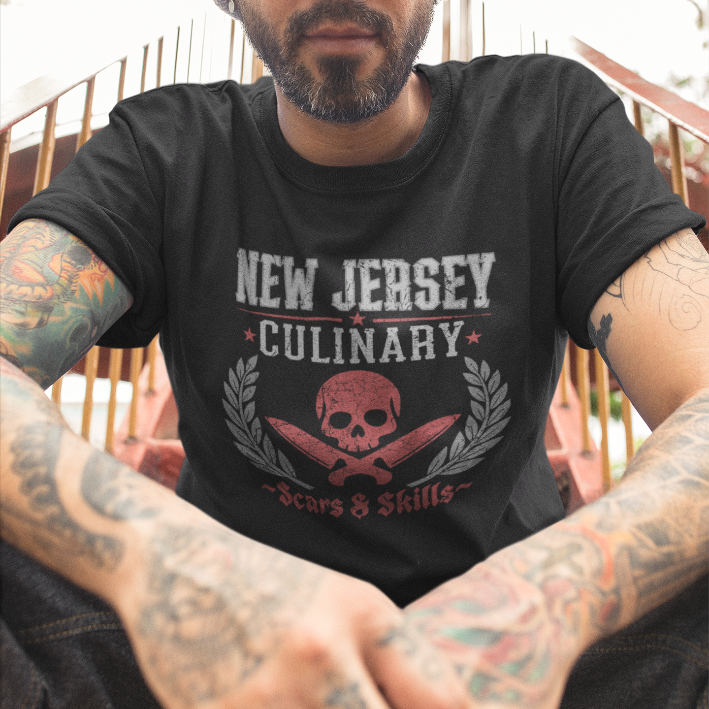 Man wearing a black t-shirt with 'New Jersey Culinary' design, sitting outdoors.
