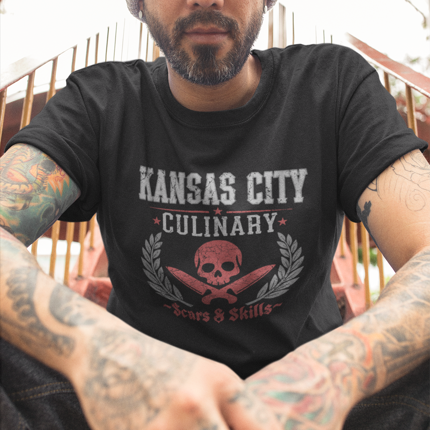 Man wearing a black t-shirt with 'Kansas City Culinary' design, sitting outdoors.
