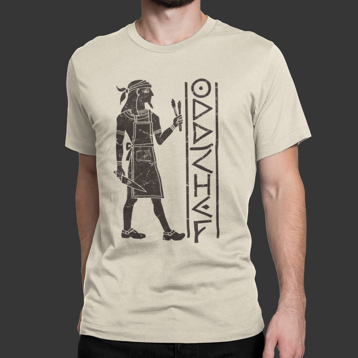 A man wearing a light beige crewneck t-shirt with a black graphic print of an ancient Egyptian figure and the word 'OANAIVA'.