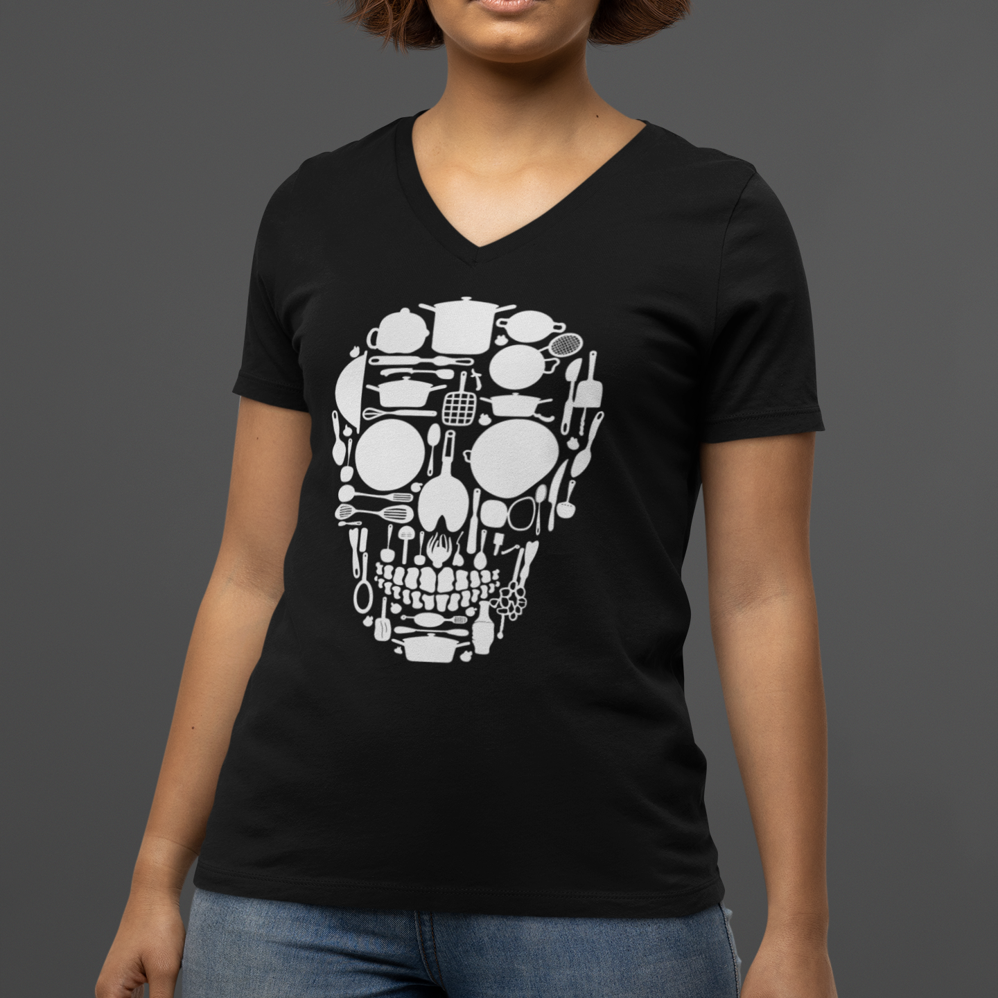 A woman wearing a black V-neck t-shirt with a white robotic skull graphic on the front, paired with blue jeans, set against a solid dark gray background.