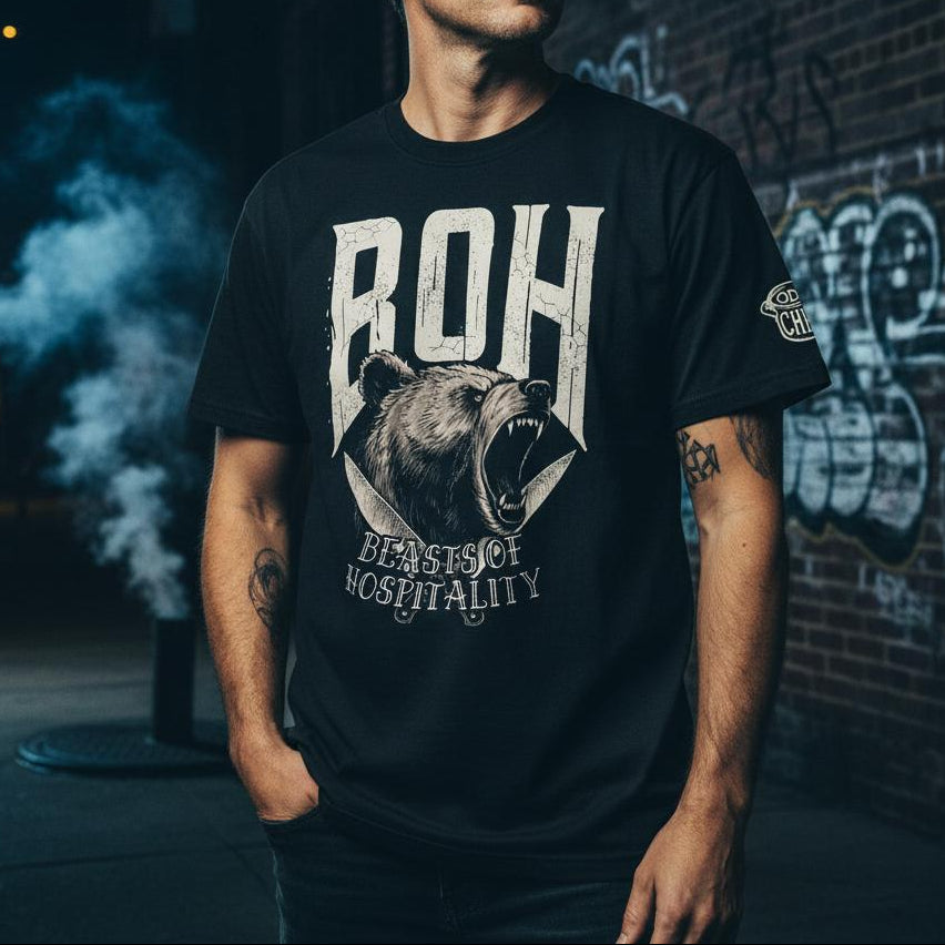 Man wearing a black t-shirt with a bear graphic and text, standing against a graffiti-covered wall.