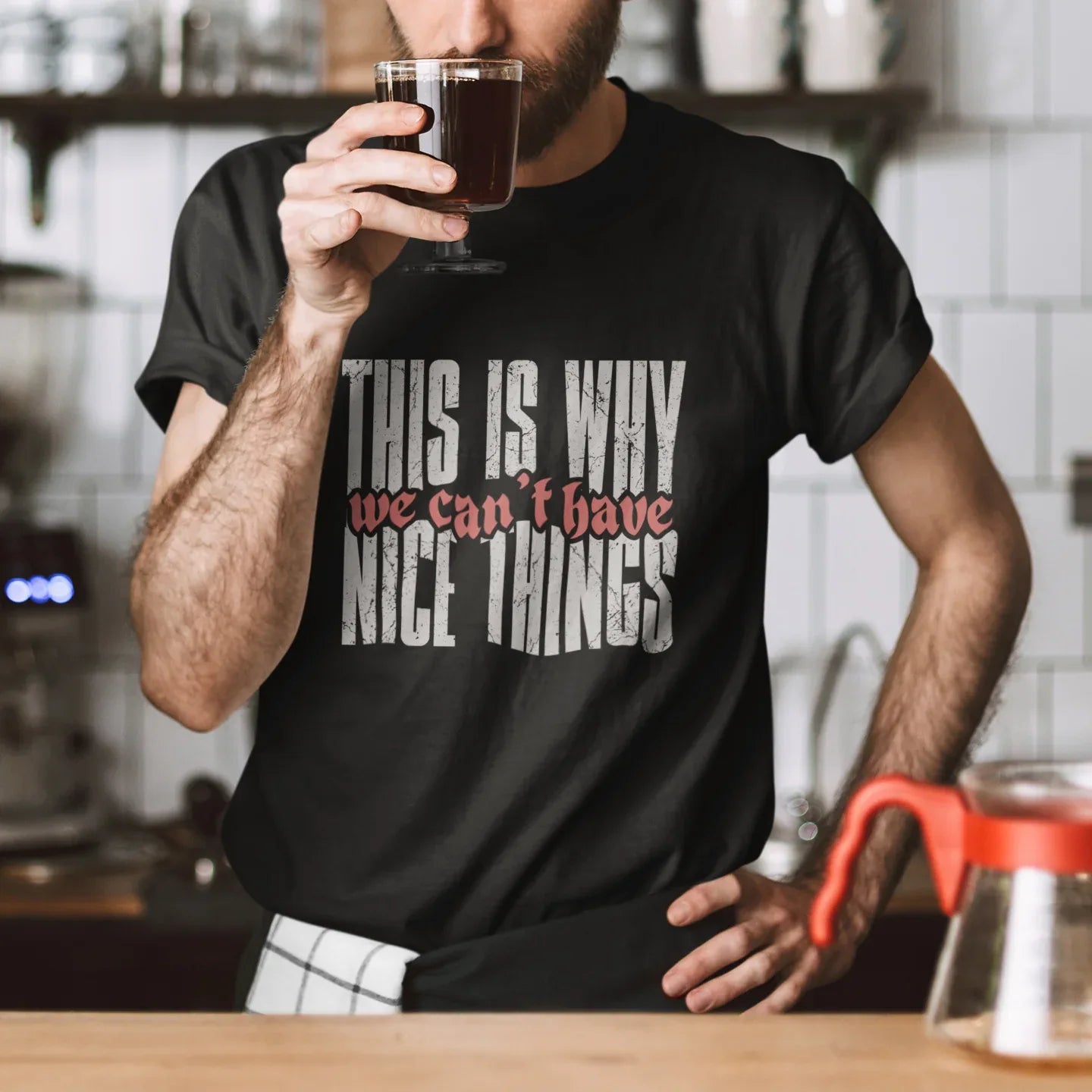 Man drinking coffee wearing a black t-shirt with text in a kitchen setting