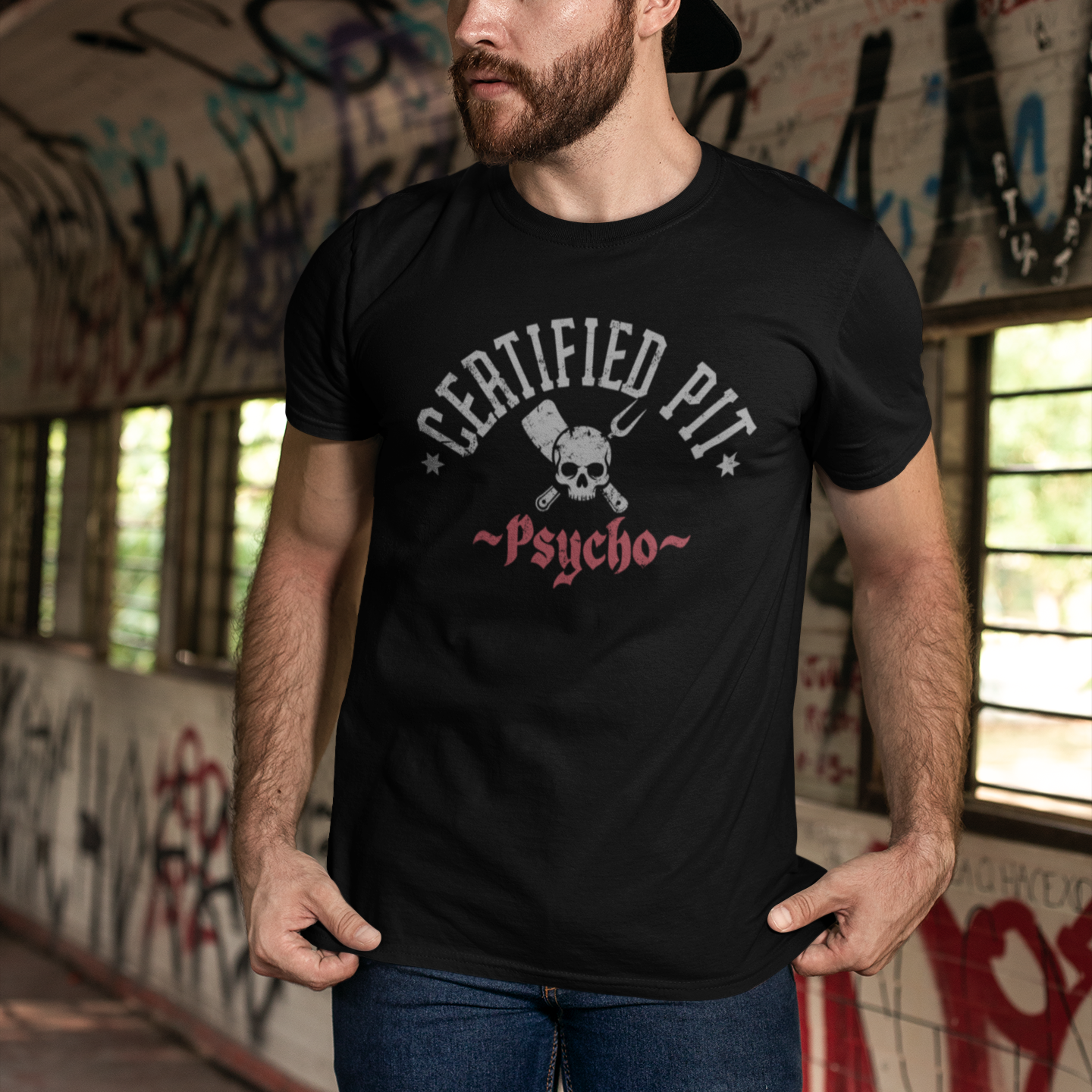 Man wearing a black t-shirt with 'Certified Pit Psycho' design in an urban setting with graffiti.