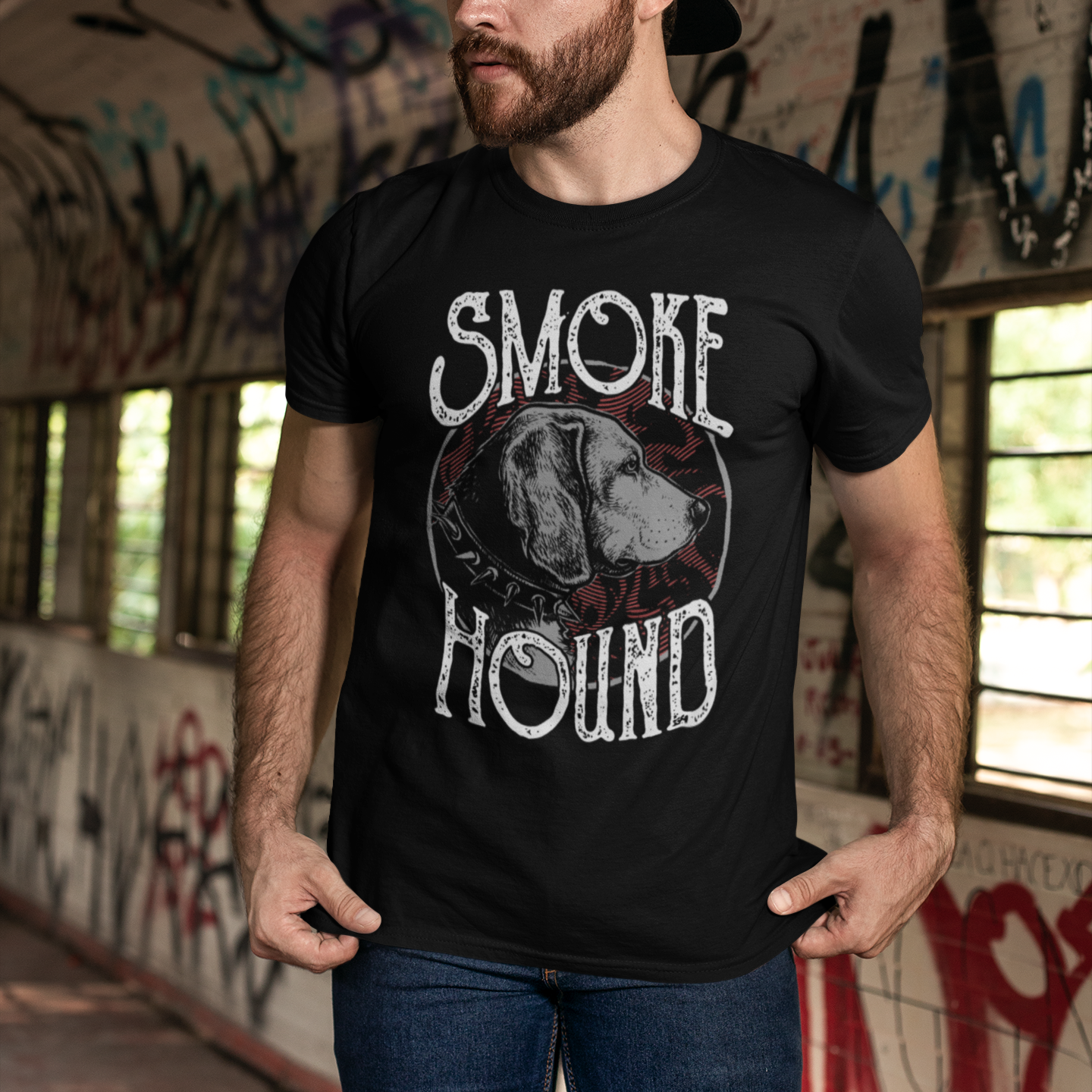 Man wearing a black t-shirt with 'Smoke Hound' graphic design in an urban setting with graffiti.