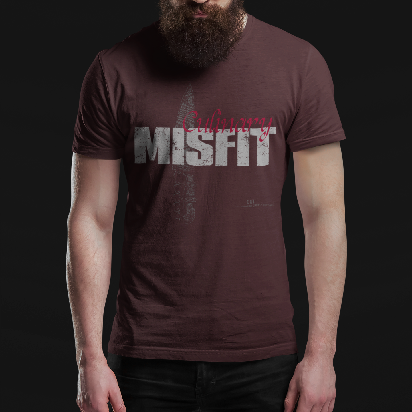 A man with a full beard and sunglasses wearing a dark brown t-shirt with a distressed graphic that reads 'Ordinary Misfit' in gray and red, set against a solid black background.