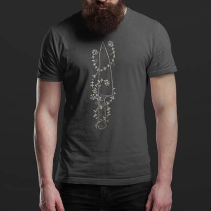 A man with a full beard and sunglasses wearing a dark gray t-shirt with a white line art graphic of a dagger surrounded by flowers, set against a dark gray background.