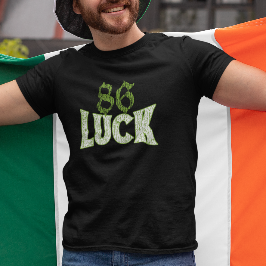 Man wearing a black t-shirt with '86 Luck' text, holding a green and orange flag.