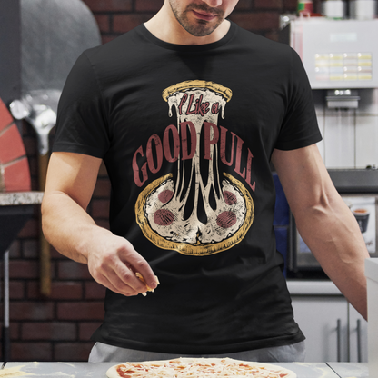A man wearing a black graphic t-shirt with a dripping pizza design and the text 'I live in GOOD RULL' stands in a pizza kitchen, sprinkling cheese onto a pizza on a counter.