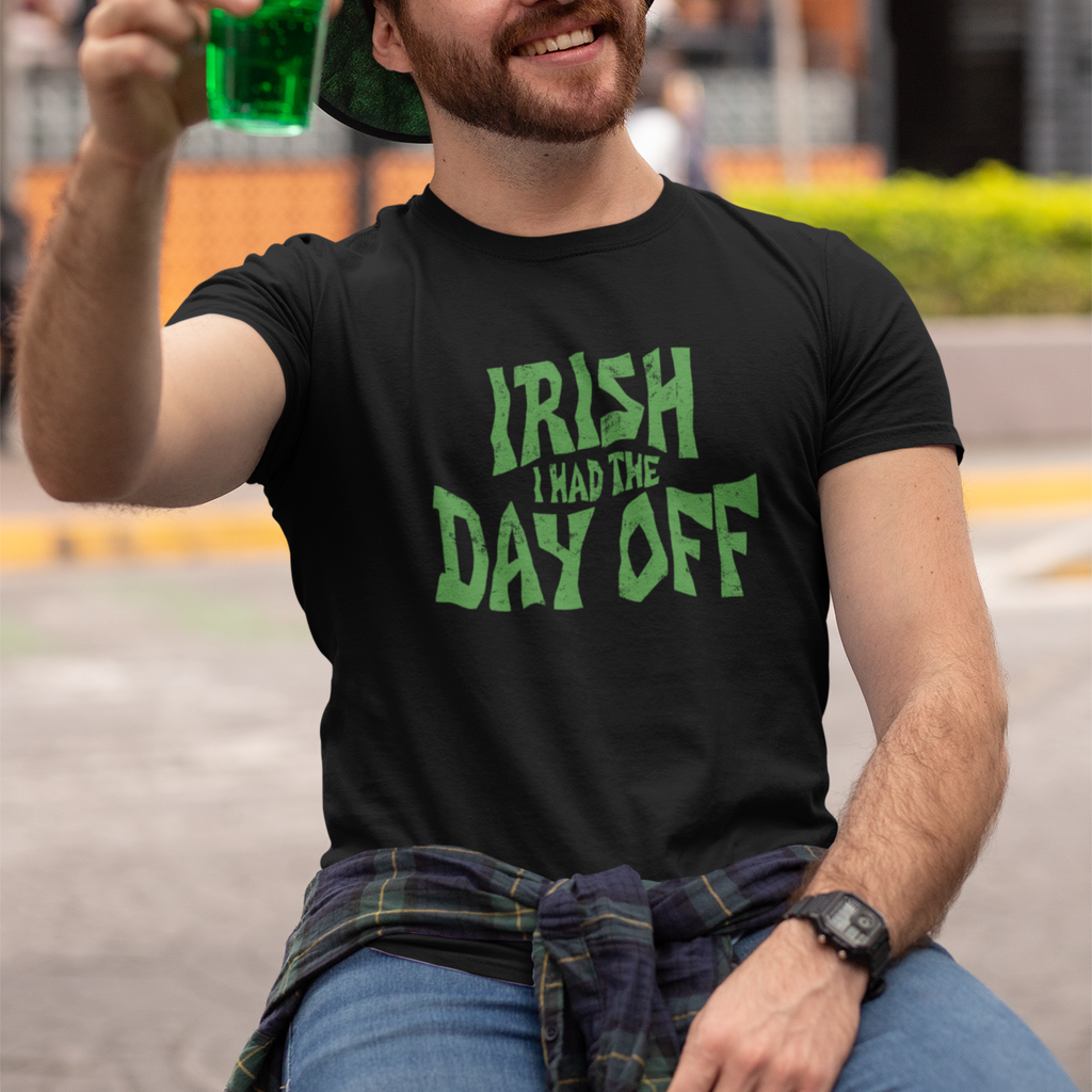 Man wearing a black t-shirt with 'Irish I Had the Day Off' text, holding a green drink, sitting outdoors.