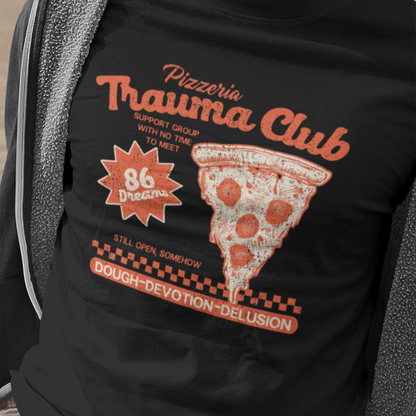 A man wearing a black graphic t-shirt with a retro pizza slice design and the text 'Pizzeria Trauma Club' and '86 Dreams'.