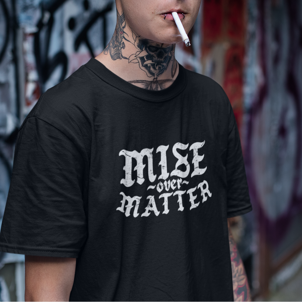Man wearing a black t-shirt with 'MISE over MATTER' text, standing in front of a graffiti-covered wall.