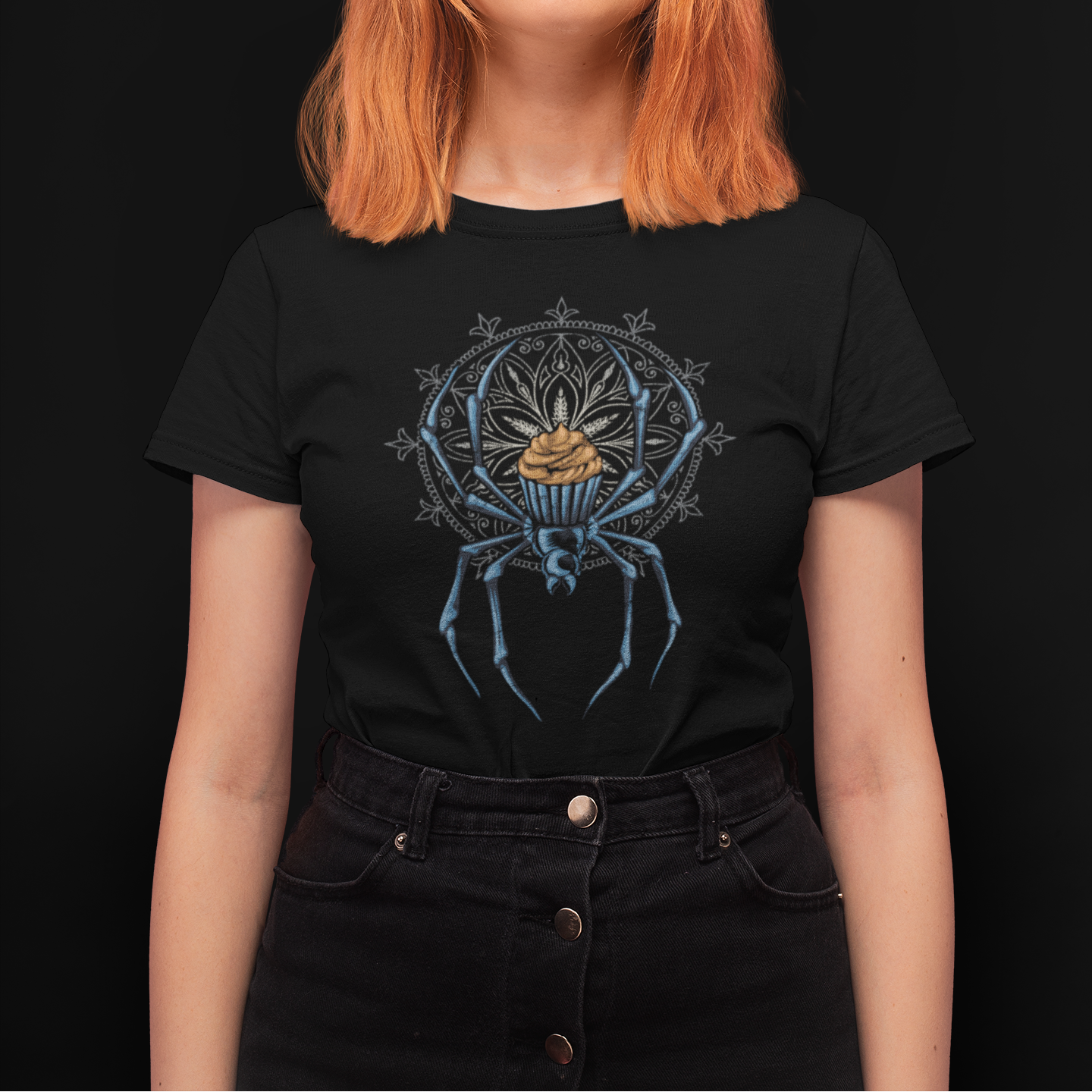 A woman with bright orange hair wearing a black graphic t-shirt featuring a blue spider design with a gold crown, set against a solid black background.