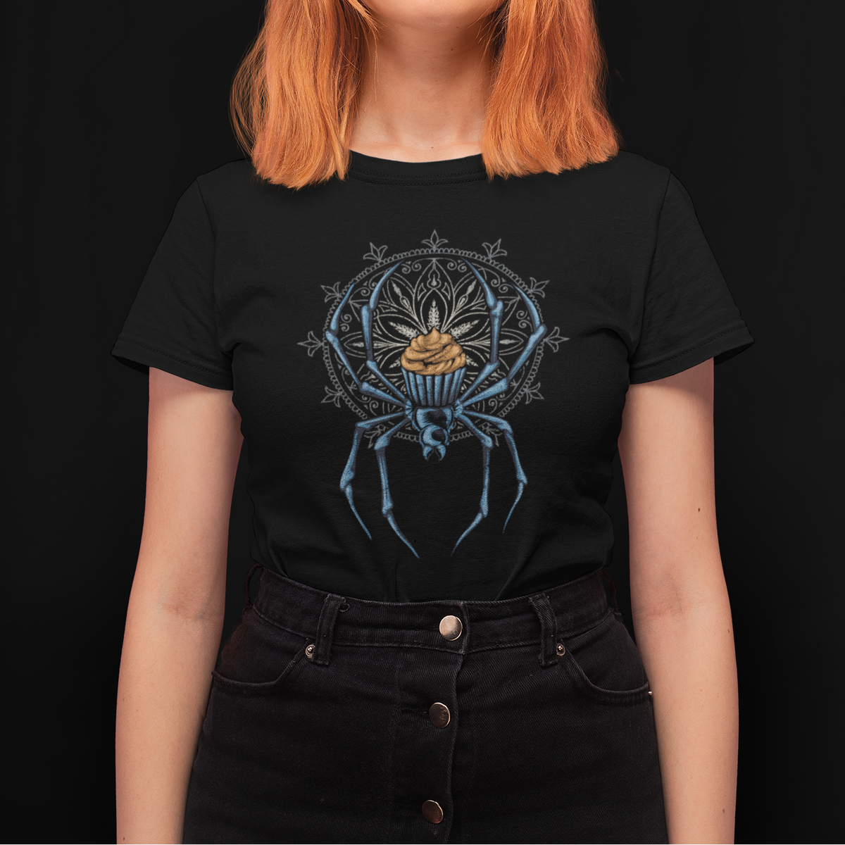 A woman with bright orange hair wearing a black graphic t-shirt featuring a blue spider design with a gold crown, set against a solid black background.